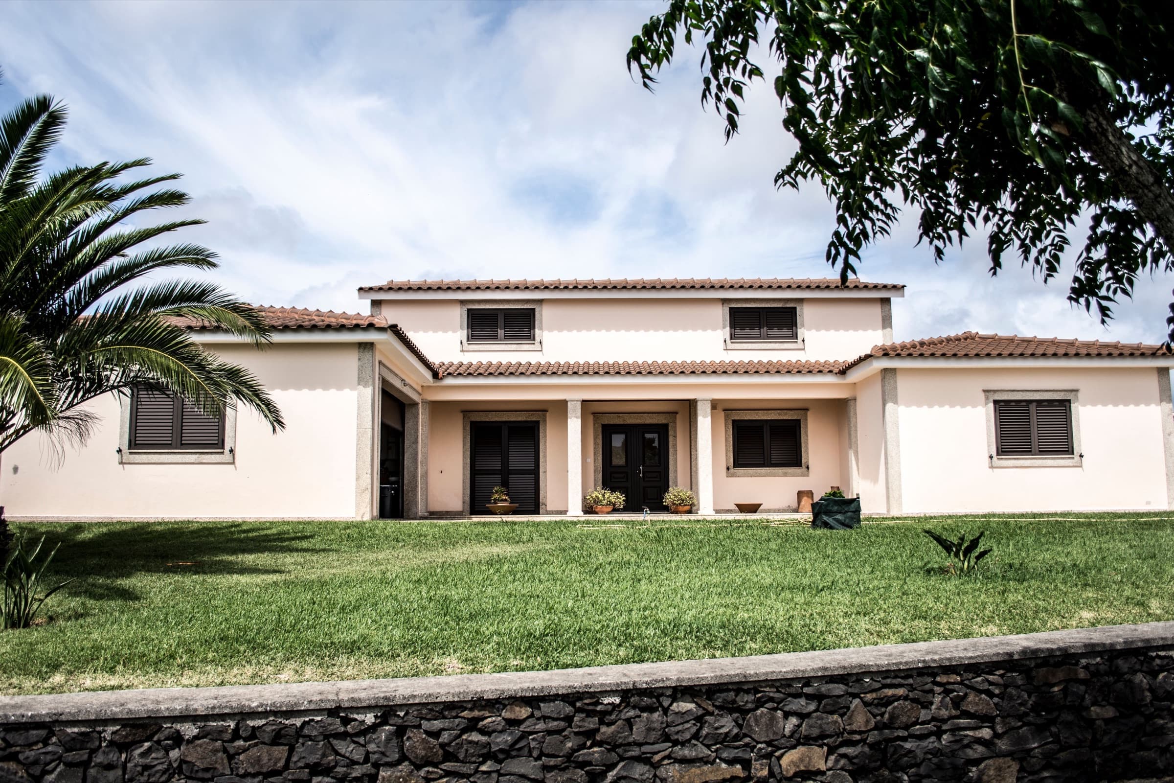 Single-story stucco home with a tile roof, a wide green lawn and a palm tree in the front yard, the kind of setting we work with for landscaping in Olmito, TX