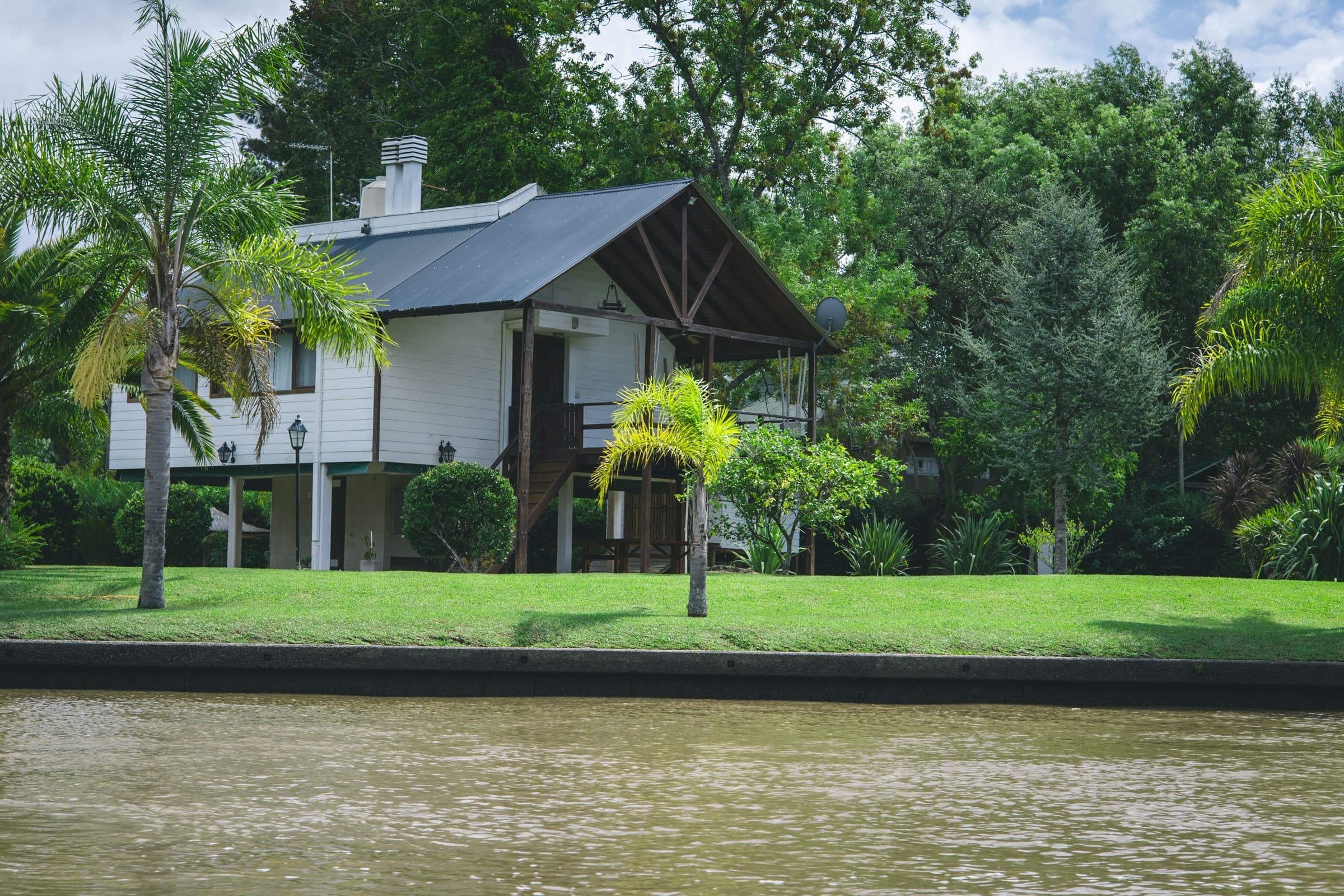 Home with a mowed lawn, palms and shade trees along the bank of a calm channel, the kind of setting we work with for landscaping in San Benito, TX